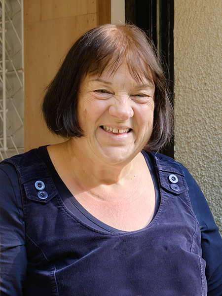 Woman with short brown hair smiling, wearing a navy top, standing outside in sunlight.