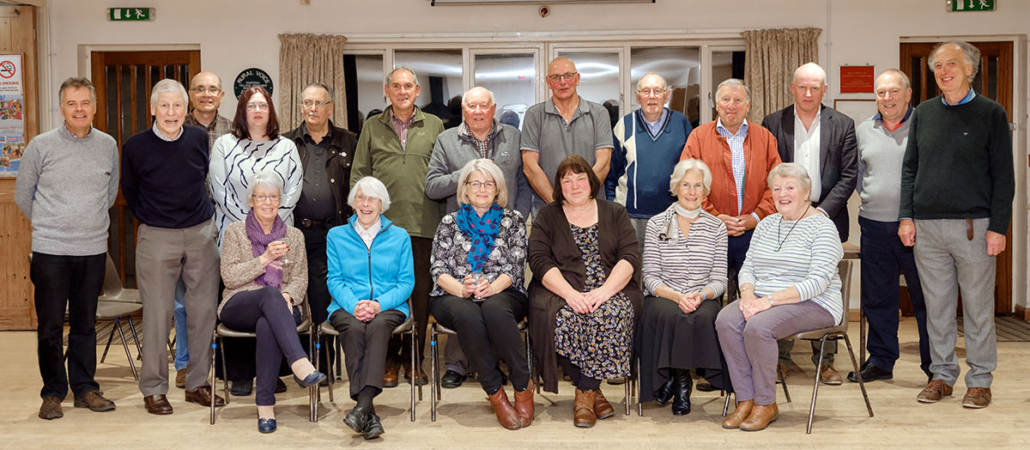 A group of older adults pose together indoors, with some seated and others standing behind them.